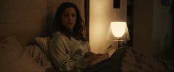 Movie still from “Dumb Money” (2023), directed by Craig Gillespie – A woman sitting in a chair holding a book; Medium shot, Over the shoulder angle