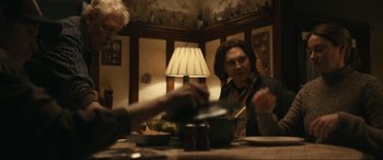 Movie still from “Dumb Money” (2023), directed by Craig Gillespie – Two people sitting at a dinner table with a lamp in the background; Medium shot, Over the shoulder angle