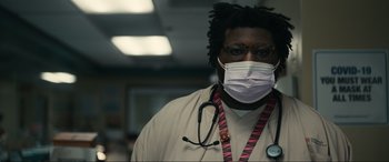 Movie still from “Dumb Money” (2023), directed by Craig Gillespie – A person wearing a face mask with a stethoscope around his neck; Close Up shot, Low angle
