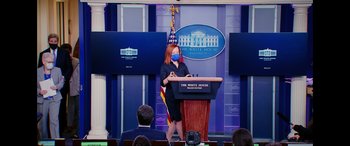 Movie still from “Dumb Money” (2023), directed by Craig Gillespie – A woman wearing a face mask stands at a podium in front of the white house; Wide shot, Low angle