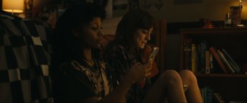 Movie still from “Dumb Money” (2023), directed by Craig Gillespie – Two women sitting on a couch looking at their phones; Medium shot, High angle