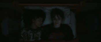Movie still from “Dumb Money” (2023), directed by Craig Gillespie – Two children in a bed with one girl looking at the camera; Medium shot, Overhead angle