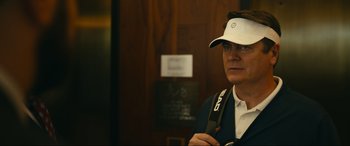 Movie still from “Dumb Money” (2023), directed by Craig Gillespie – A man in a white hat holding a tennis racquet; Close Up shot, Over the shoulder angle