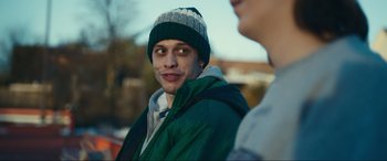 Movie still from “Dumb Money” (2023), directed by Craig Gillespie – A young man wearing a green jacket and a hat; Close Up shot, Over the shoulder angle