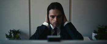Movie still from “Dumb Money” (2023), directed by Craig Gillespie – A man in a suit and tie holding his hands to his ears; Close Up shot, High angle