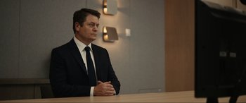 Movie still from “Dumb Money” (2023), directed by Craig Gillespie – A man in a suit and tie sitting at a table; Medium shot, Low angle