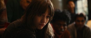 Movie still from “Dumb Money” (2023), directed by Craig Gillespie – A young woman with long hair and a brown jacket; Close Up shot, Over the shoulder angle