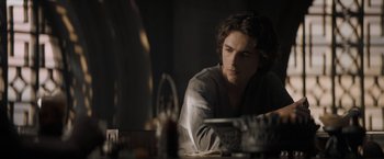 Movie still from “Dune” (2021), directed by Denis Villeneuve – A man sitting at a dinner table looking at a plate of food; Medium shot, Low angle