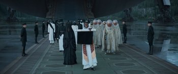 Movie still from “Dune” (2021), directed by Denis Villeneuve – A man holding a sign in front of a group of people; Wide shot, Over the shoulder angle
