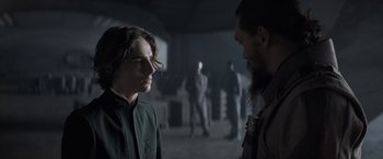 Movie still from “Dune” (2021), directed by Denis Villeneuve – A man and a woman are standing in a dark room; Medium shot, Over the shoulder angle