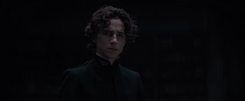 Movie still from “Dune” (2021), directed by Denis Villeneuve – A young man with curly hair wearing a black suit; Close Up shot, Low angle