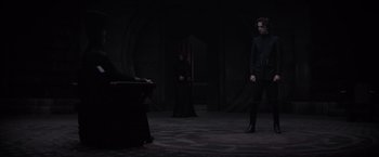 Movie still from “Dune” (2021), directed by Denis Villeneuve – Two people in black clothes are standing in a dark room; Wide shot, Over the shoulder angle