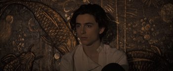 Movie still from “Dune” (2021), directed by Denis Villeneuve – A young man is sitting in front of a wall; Close Up shot, High angle