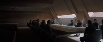 Movie still from “Dune” (2021), directed by Denis Villeneuve – A group of men sitting at a long table in a room; Wide shot, High angle