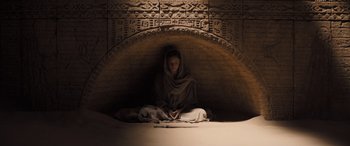 Movie still from “Dune” (2021), directed by Denis Villeneuve – A person sitting in a cave with a blanket draped over their head; Wide shot, High angle