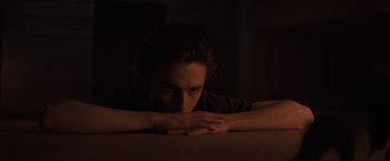 Movie still from “Dune” (2021), directed by Denis Villeneuve – A man sitting at a table in the dark with his head resting on his hands; Medium shot, High angle