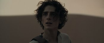 Movie still from “Dune” (2021), directed by Denis Villeneuve – A young man with long dark hair looking at the camera; Close Up shot, Over the shoulder angle