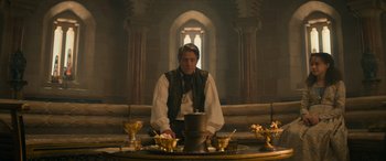 Movie still from “Dungeons & Dragons: Honor Among Thieves” (2023), directed by John Francis Daley – A man sitting in front of a table with a hat on it; Medium shot, Low angle