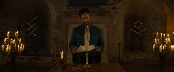 Movie still from “Dungeons & Dragons: Honor Among Thieves” (2023), directed by John Francis Daley – A man sitting in front of an open book in front of a lit candle; Medium shot, Low angle