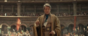 Movie still from “Dungeons & Dragons: Honor Among Thieves” (2023), directed by John Francis Daley – An older man wearing a robe and a necklace; Medium shot, Over the shoulder angle