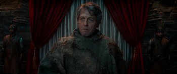 Movie still from “Dungeons & Dragons: Honor Among Thieves” (2023), directed by John Francis Daley – A man in a costume is standing in front of a red curtain; Medium shot, Low angle