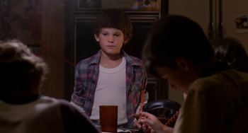 Movie still from “E.T. the Extra-Terrestrial” (1982), directed by Steven Spielberg – A young man sitting at a table with a glass of water; Medium shot, Over the shoulder angle