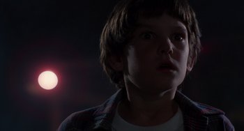 Movie still from “E.T. the Extra-Terrestrial” (1982), directed by Steven Spielberg – A young boy stares into the distance in front of a red light; Close Up shot, Low angle