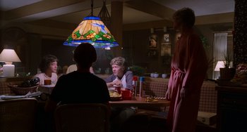 Movie still from “E.T. the Extra-Terrestrial” (1982), directed by Steven Spielberg – A woman sitting at a dinner table with two other women; Medium shot, Over the shoulder angle