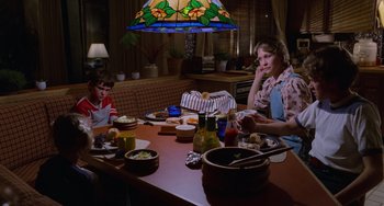 Movie still from “E.T. the Extra-Terrestrial” (1982), directed by Steven Spielberg – A woman sitting at a dinner table with two children; Medium shot, High angle
