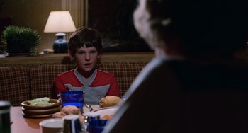 Movie still from “E.T. the Extra-Terrestrial” (1982), directed by Steven Spielberg – A young boy sitting at a dinner table with a woman; Medium shot, Over the shoulder angle
