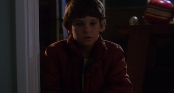 Movie still from “E.T. the Extra-Terrestrial” (1982), directed by Steven Spielberg – A boy in a red jacket is sitting in a dark room; Close Up shot, High angle
