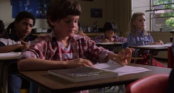 Movie still from “E.T. the Extra-Terrestrial” (1982), directed by Steven Spielberg – A young boy sitting at a desk writing on a piece of paper; Medium shot, High angle