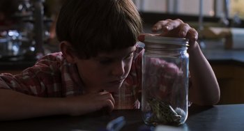 Movie still from “E.T. the Extra-Terrestrial” (1982), directed by Steven Spielberg – A young boy looking at a jar of coins on a table; Close Up shot, Over the shoulder angle