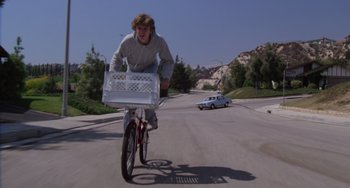 Movie still from “E.T. the Extra-Terrestrial” (1982), directed by Steven Spielberg – A man riding a bike down a street with a basket on the back of the bike; Wide shot, Low angle