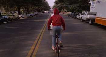 Movie still from “E.T. the Extra-Terrestrial” (1982), directed by Steven Spielberg – A man riding a bike down the middle of the street; Wide shot, High angle