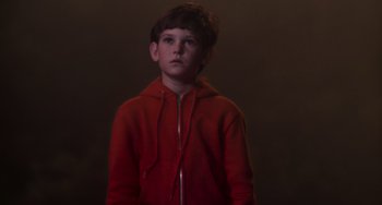 Movie still from “E.T. the Extra-Terrestrial” (1982), directed by Steven Spielberg – A young boy in a red hoodie standing in a dark room; Medium shot, Low angle