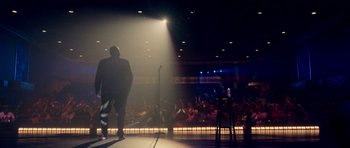 Movie still from “Chappelle's Home Team - Earthquake: Legendary” (2022), directed by Stan Lathan – A man standing on a stage in front of an audience; Wide shot, Over the shoulder angle