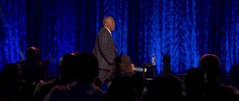 Movie still from “Chappelle's Home Team - Earthquake: Legendary” (2022), directed by Stan Lathan – A man standing on a stage in front of an audience; Wide shot, Over the shoulder angle