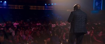 Movie still from “Chappelle's Home Team - Earthquake: Legendary” (2022), directed by Stan Lathan – A man standing on a stage in front of an audience; Wide shot, Over the shoulder angle
