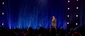 Movie still from “Chappelle's Home Team - Earthquake: Legendary” (2022), directed by Stan Lathan – A man standing on a stage in front of an audience; Extreme Wide shot, Over the shoulder angle