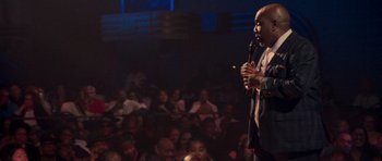Movie still from “Chappelle's Home Team - Earthquake: Legendary” (2022), directed by Stan Lathan – A man standing on a stage holding a microphone; Medium shot, High angle