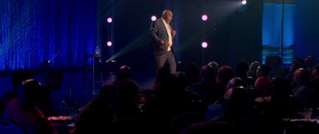 Movie still from “Chappelle's Home Team - Earthquake: Legendary” (2022), directed by Stan Lathan – A man standing on a stage in front of an audience; Wide shot, Over the shoulder angle