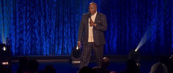 Movie still from “Chappelle's Home Team - Earthquake: Legendary” (2022), directed by Stan Lathan – A man standing on a stage holding a microphone; Extreme Wide shot, Over the shoulder angle