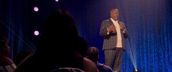 Movie still from “Chappelle's Home Team - Earthquake: Legendary” (2022), directed by Stan Lathan – A man standing on a stage holding a microphone; Medium shot, Over the shoulder angle