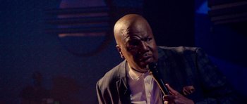 Movie still from “Chappelle's Home Team - Earthquake: Legendary” (2022), directed by Stan Lathan – A man with a microphone in his mouth; Close Up shot, Low angle