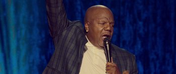 Movie still from “Chappelle's Home Team - Earthquake: Legendary” (2022), directed by Stan Lathan – A man with a microphone in his hand; Medium shot, Low angle