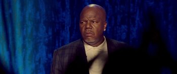 Movie still from “Chappelle's Home Team - Earthquake: Legendary” (2022), directed by Stan Lathan – A bald man in a suit and tie looking angry; Close Up shot, Low angle