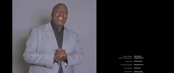 Movie still from “Chappelle's Home Team - Earthquake: Legendary” (2022), directed by Stan Lathan – A man in a gray suit clapping his hands; Medium shot, High angle