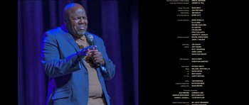 Movie still from “Chappelle's Home Team - Earthquake: Legendary” (2022), directed by Stan Lathan – An older african american man holding a microphone; Medium shot, High angle