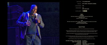 Movie still from “Chappelle's Home Team - Earthquake: Legendary” (2022), directed by Stan Lathan – A man standing on a stage holding a microphone; Medium shot, Over the shoulder angle